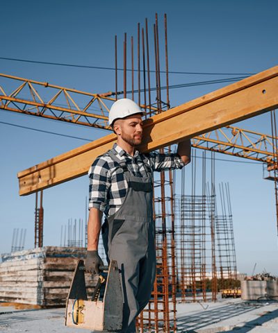 Holding big wooden piece. Man is working on the construction site at daytime.