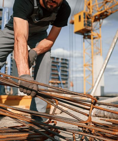 Metal pieces covered in rust. Man in uniform is working on the construction site.